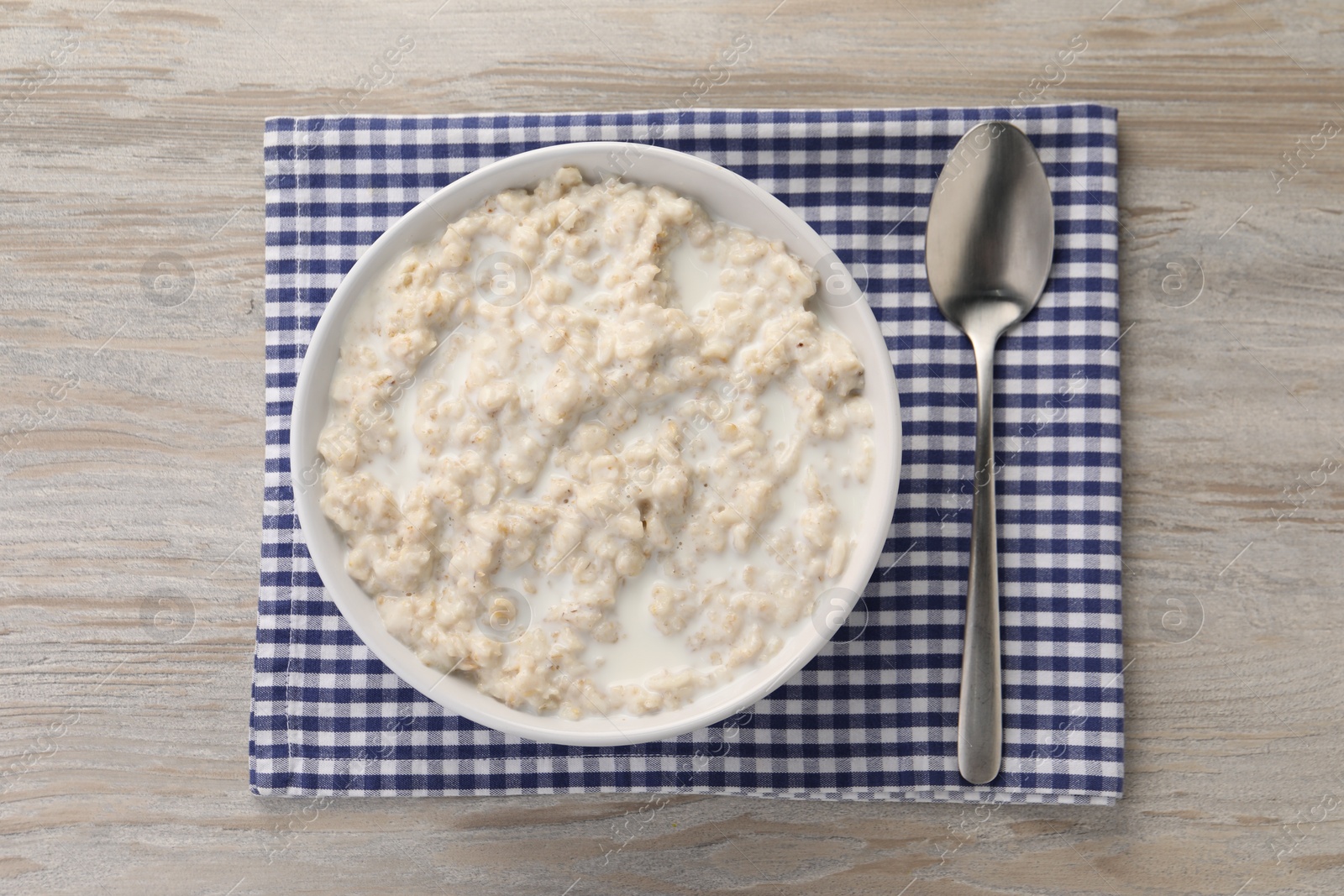 Photo of Tasty boiled oatmeal in bowl and spoon on wooden table, top view