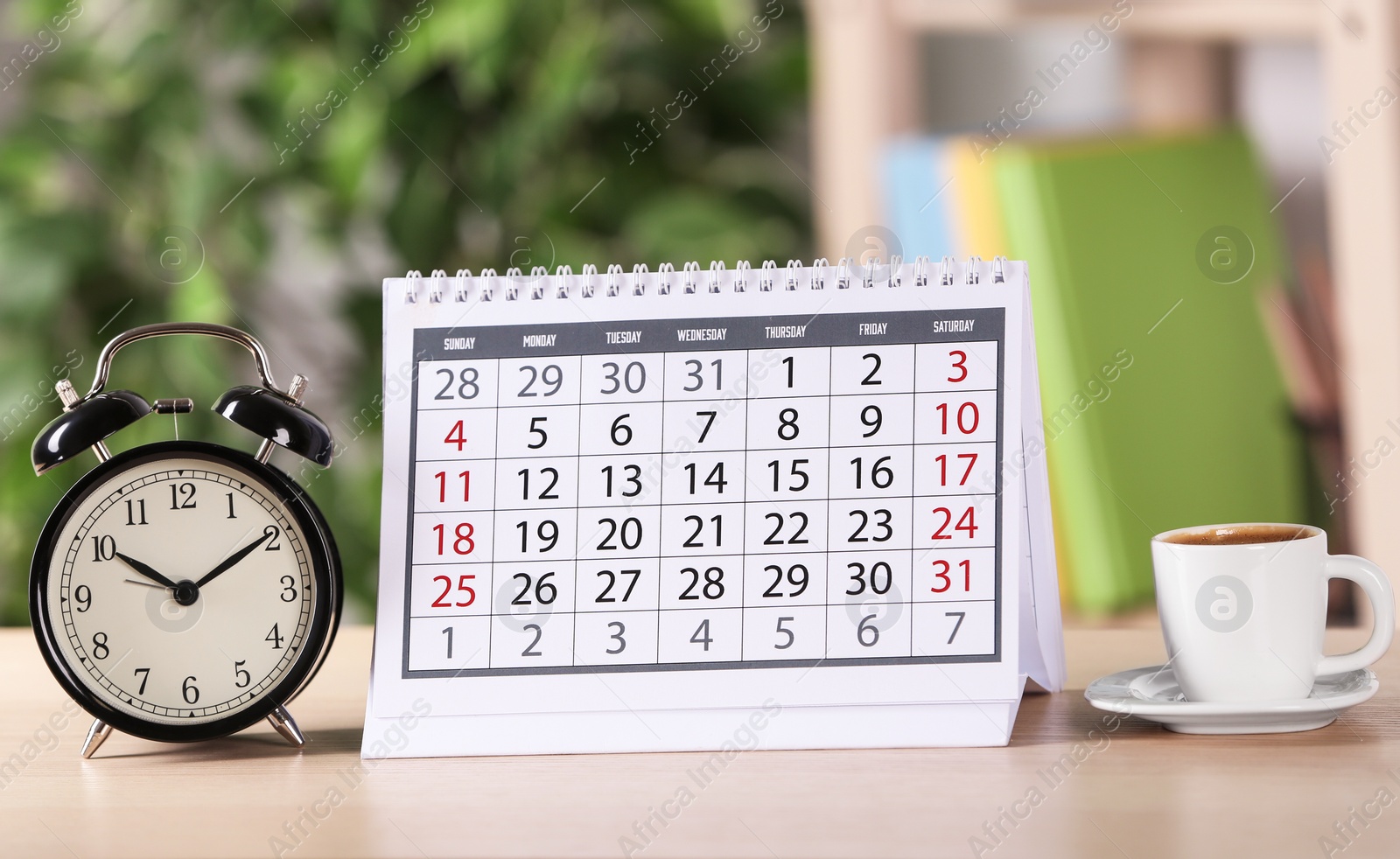 Photo of Calendar, alarm clock and cup of coffee on wooden table