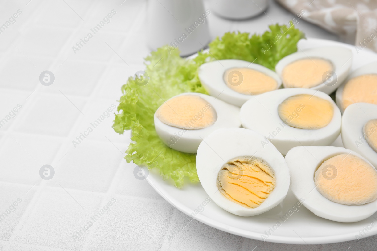 Photo of Fresh hard boiled eggs and lettuce on white tiled table, closeup. Space for text