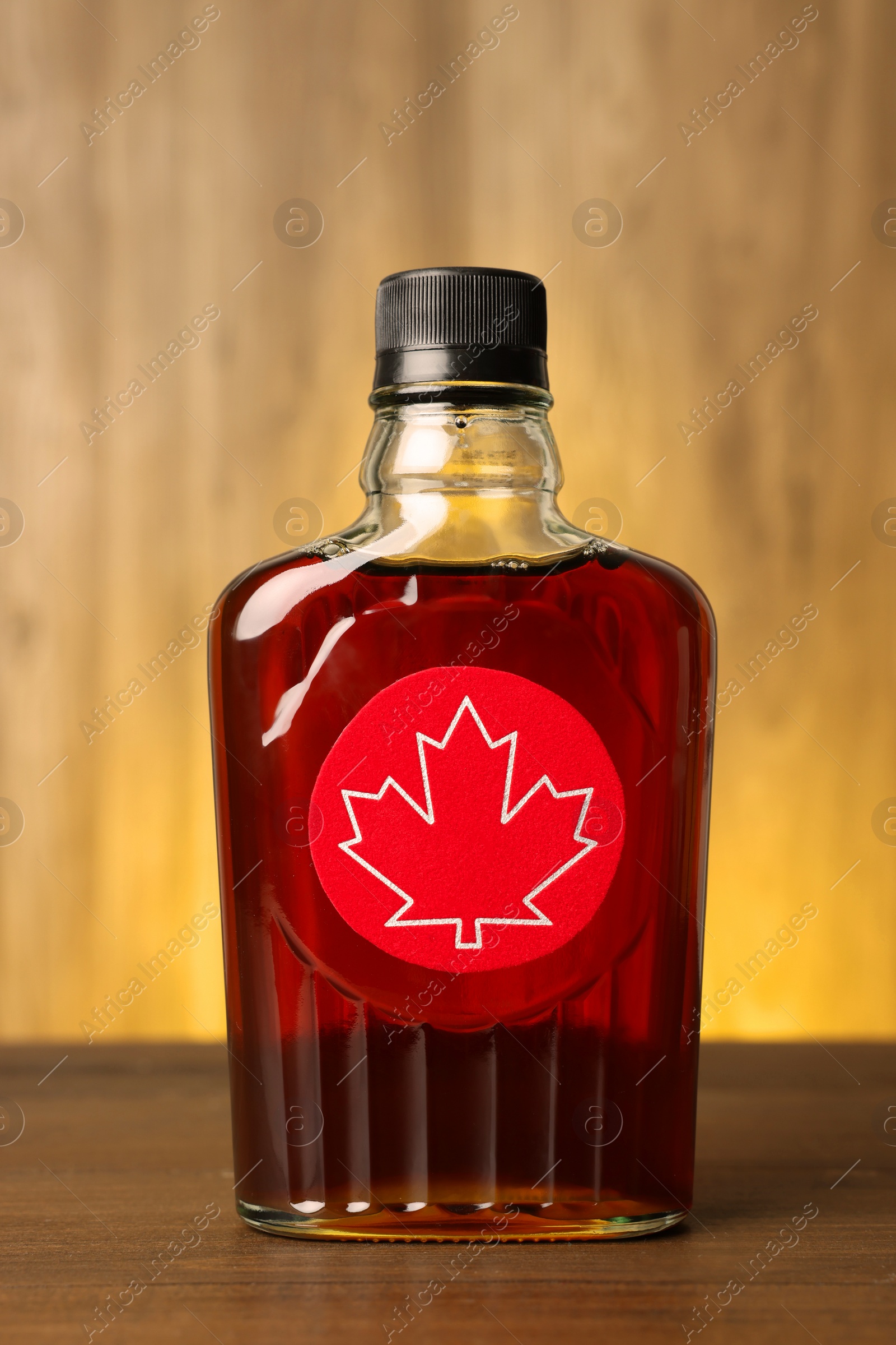 Photo of Glass bottle of tasty maple syrup on wooden table