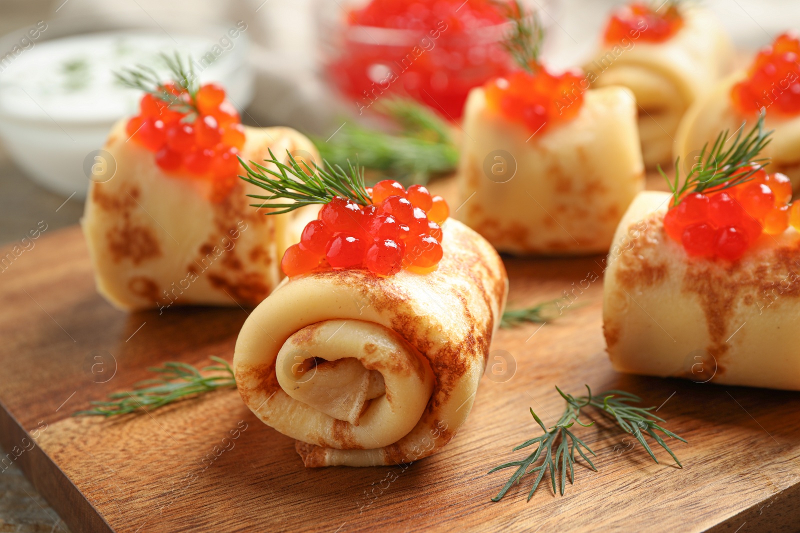 Photo of Delicious thin pancakes with red caviar on wooden board, closeup