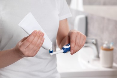 Woman squeezing toothpaste from tube onto electric toothbrush in bathroom, closeup