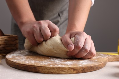 Photo of Man kneading dough at table near grey wall, closeup
