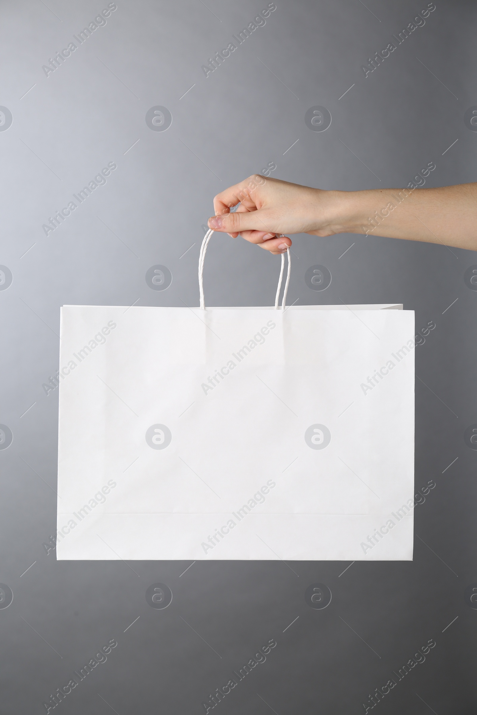 Photo of Woman holding white paper bag on grey background, closeup. Mockup for design