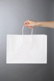 Photo of Woman holding white paper bag on grey background, closeup. Mockup for design