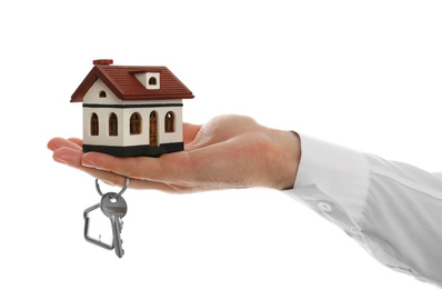 Photo of Real estate agent holding house model and key on white background, closeup