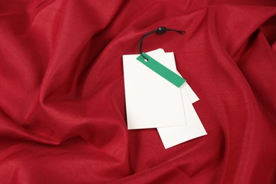 Photo of Blank white tags on red fabric. Space for text