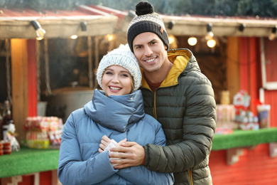 Photo of Happy couple in warm clothes at winter fair. Christmas season