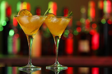 Martini glasses with cocktail, ice cubes and rosemary on counter in bar. Space for text