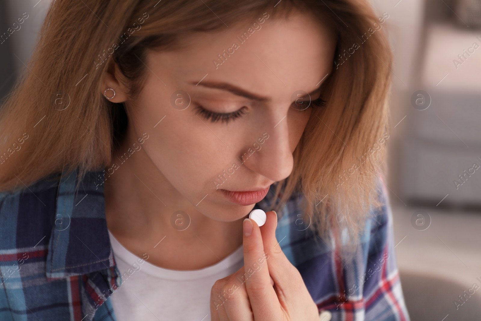 Photo of Upset young woman taking abortion pill on blurred background, closeup