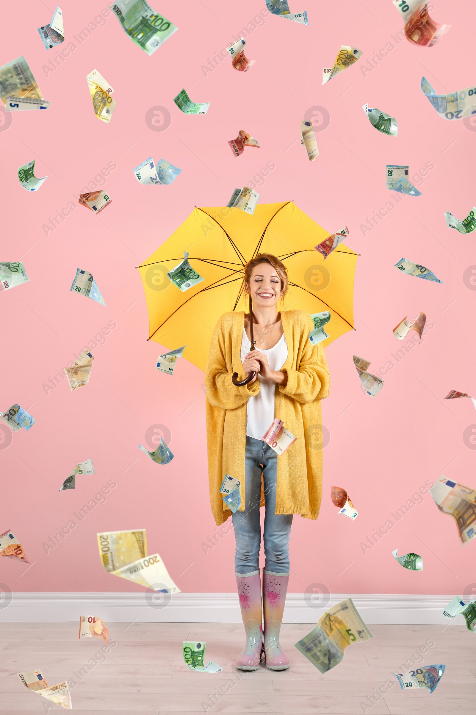 Image of Woman with yellow umbrella under money rain on color background 