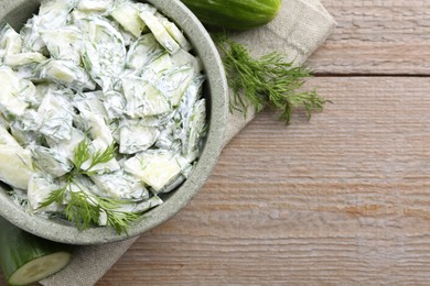 Photo of Delicious cucumber salad in bowl and ingredients on wooden table, flat lay. Space for text