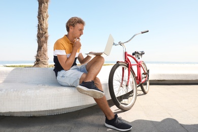 Attractive man with laptop and bike outdoors on sunny day