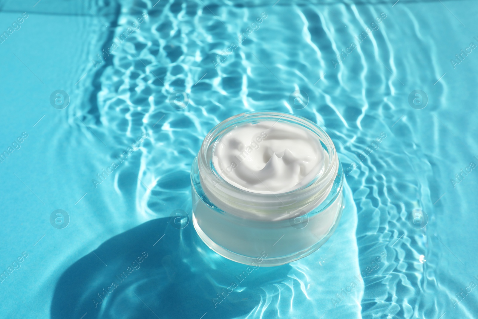 Photo of Jar with moisturizing cream in water on light blue background