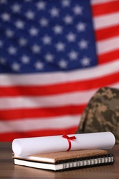 Diploma and notebooks on wooden table against flag of USA. Military education