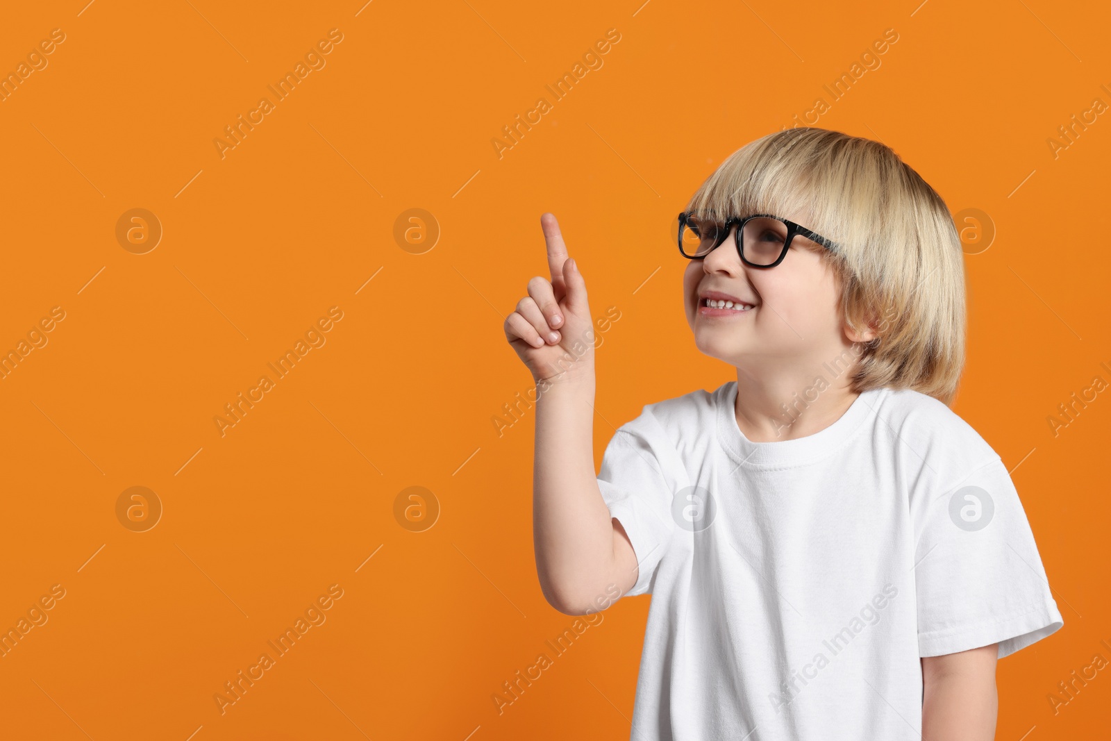 Photo of Cute little boy wearing glasses on orange background, space for text