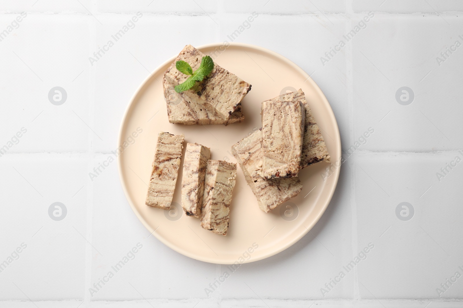 Photo of Tasty chocolate halva with mint on white tiled table, top view