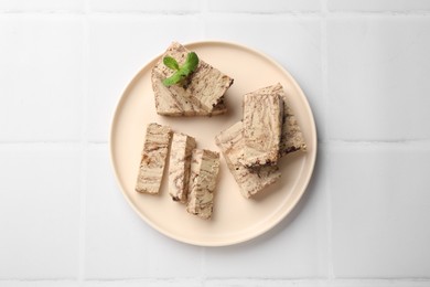 Photo of Tasty chocolate halva with mint on white tiled table, top view