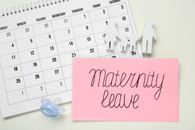 Card with phrase Maternity Leave, calendar, pacifier and figures of family on beige background, flat lay