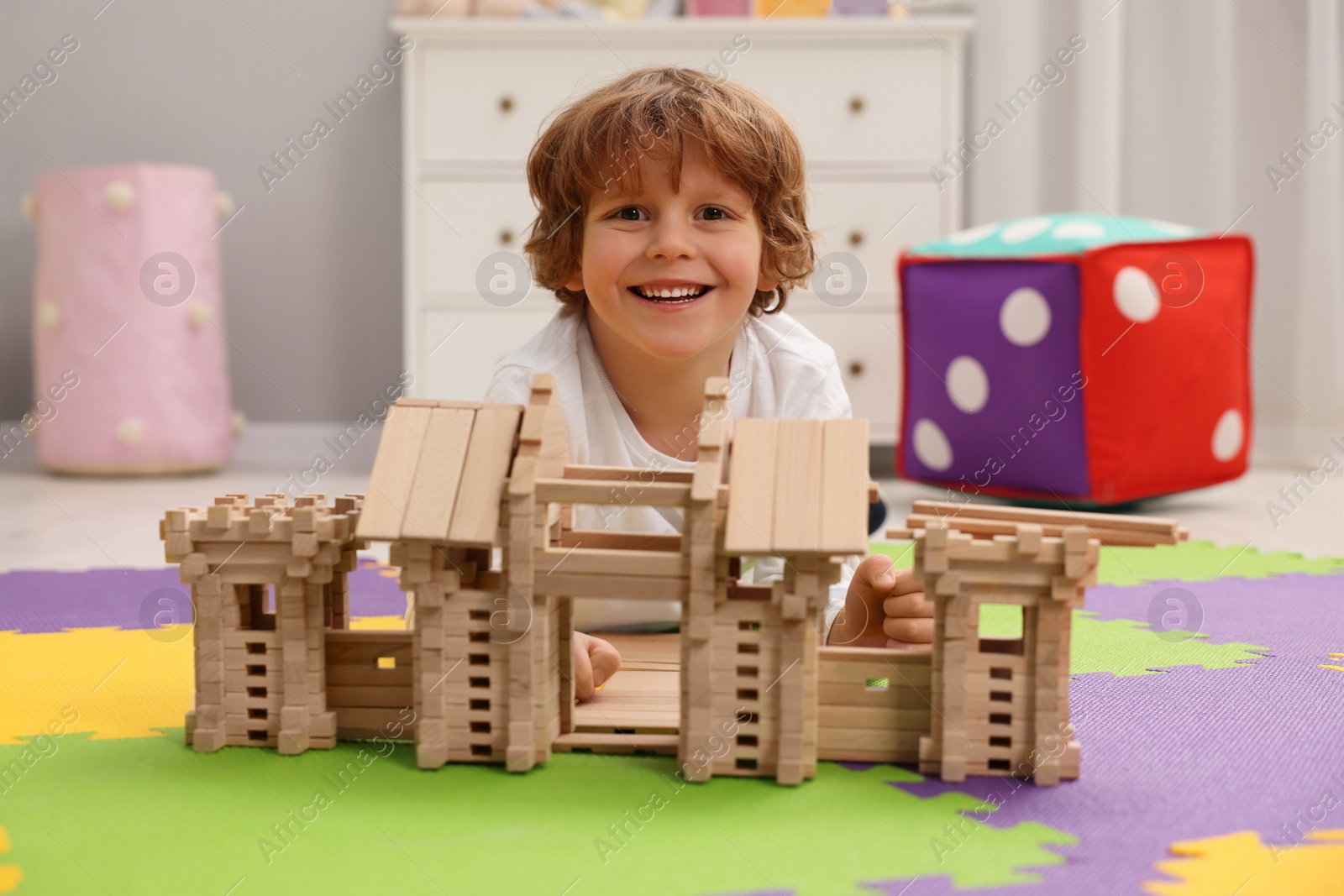 Photo of Little boy playing with wooden entry gate on puzzle mat in room. Child's toy