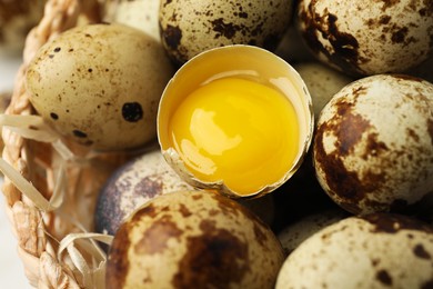 Photo of Many whole and cracked quail eggs in wicker bowl, closeup