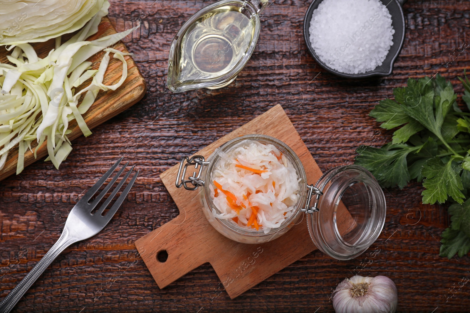 Photo of Glass jar of tasty sauerkraut and ingredients on wooden table, flat lay