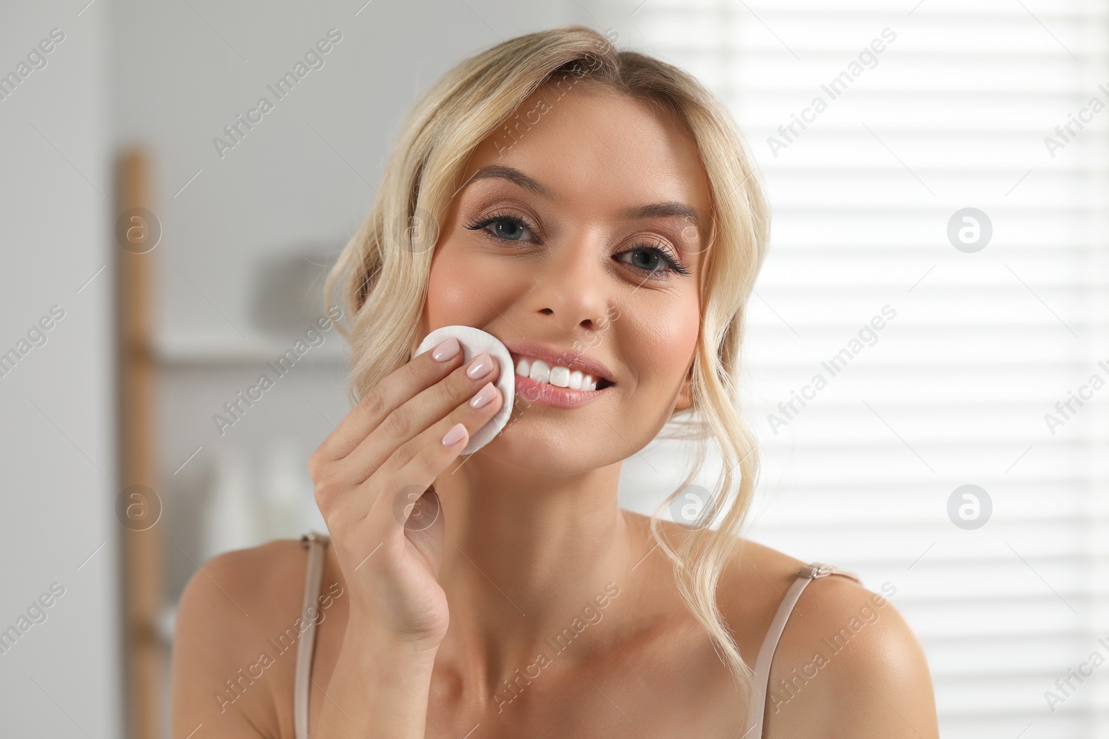 Photo of Smiling woman removing makeup with cotton pad indoors