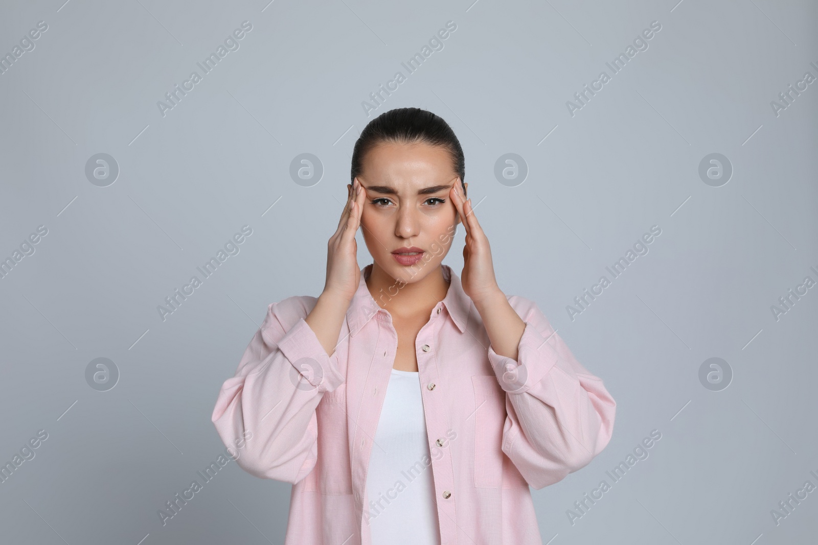 Photo of Young woman suffering from headache on light grey background