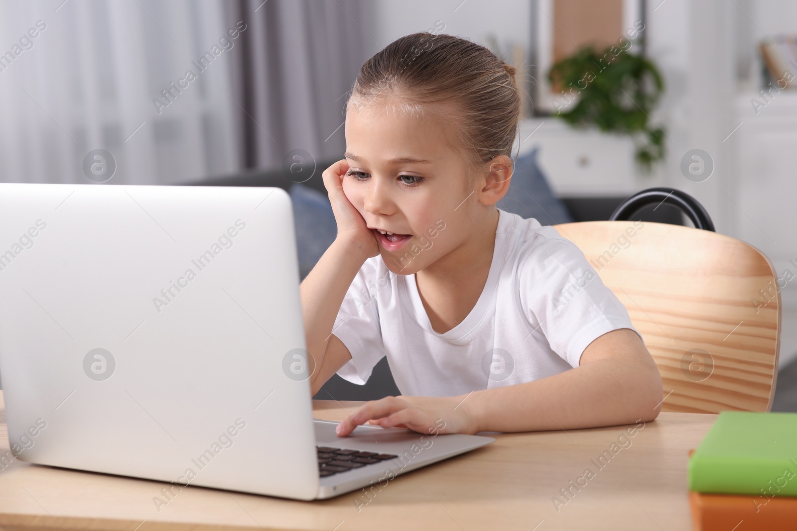 Photo of Little girl using laptop at table indoors. Internet addiction