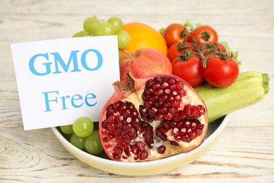 Photo of Fresh fruits, vegetables and card with text GMO Free in bowl on white wooden table