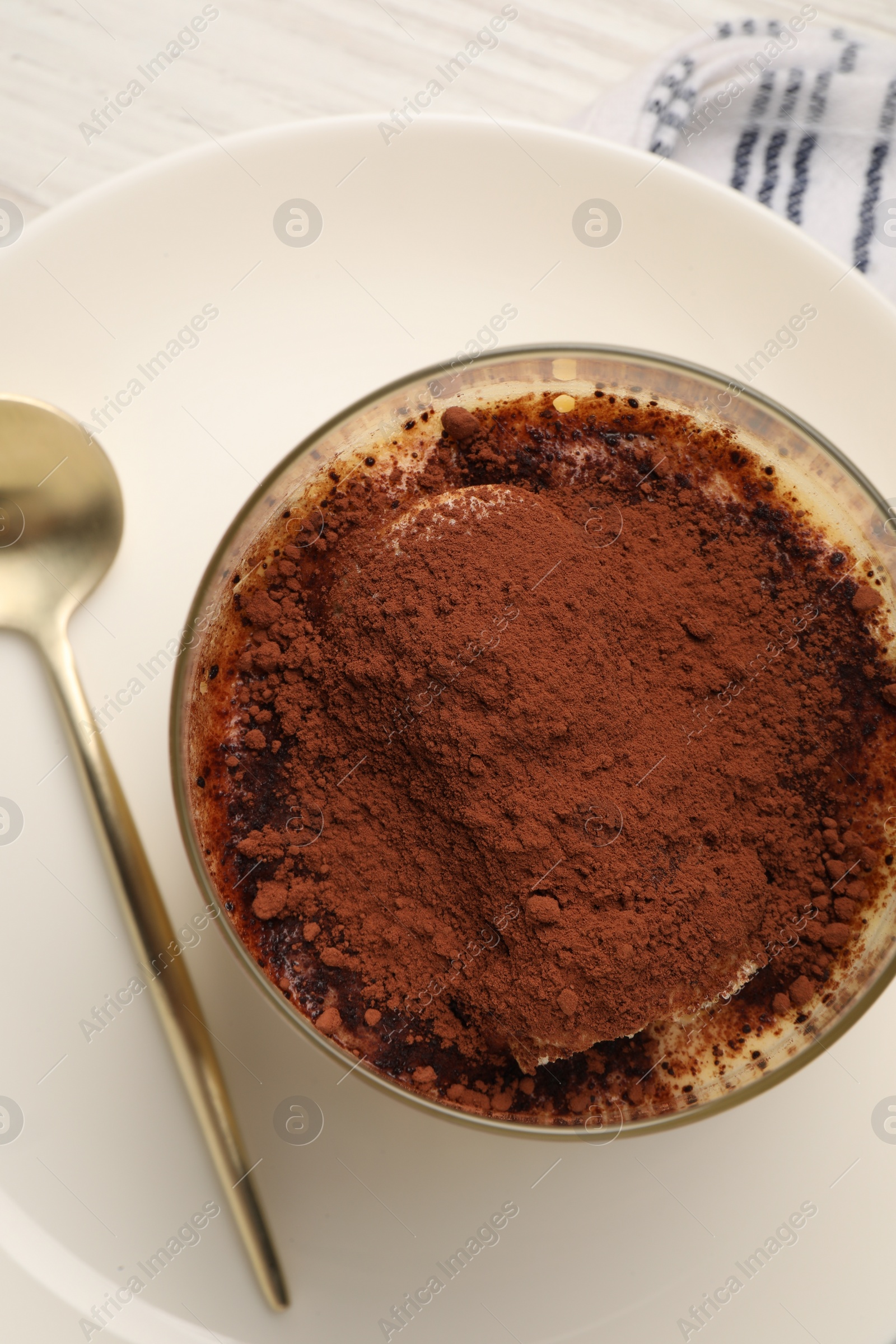 Photo of Delicious tiramisu in glass and spoon on table, top view