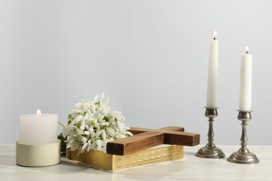 Burning church candles, wooden cross, Bible and flowers on white table