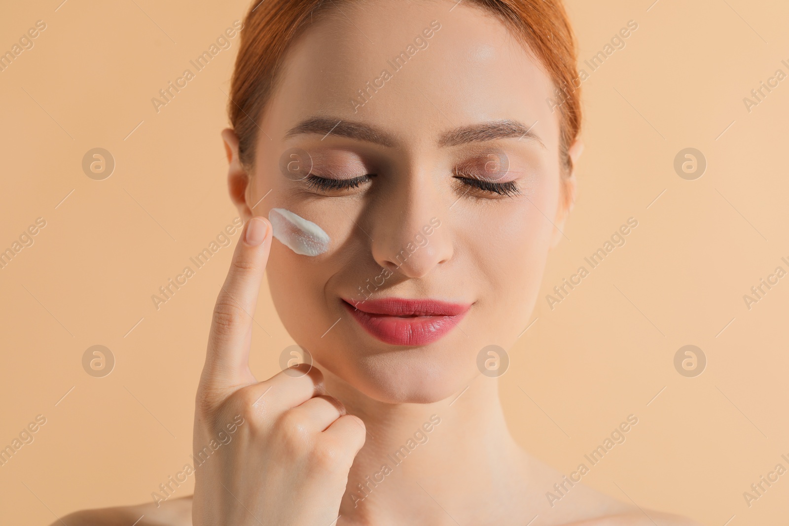 Photo of Beautiful young woman with sun protection cream on her face against beige background, closeup