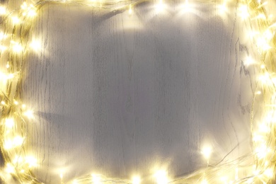 Photo of Frame of beautiful glowing Christmas lights on white wooden table, top view. Space for text