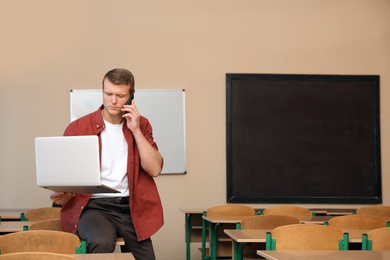 Male teacher talking on phone in modern classroom