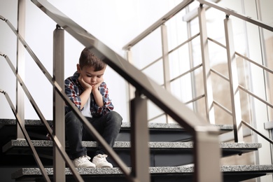 Sad little boy sitting on stairs indoors
