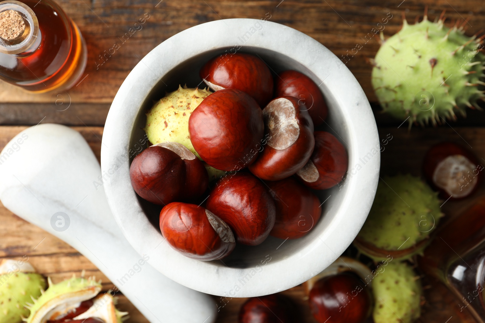 Photo of Mortar with pestle, chestnuts and essential oil on wooden table, flat lay