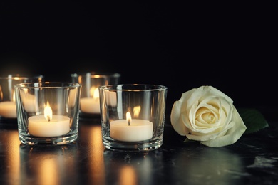 White rose and burning candles on table in darkness. Funeral symbol