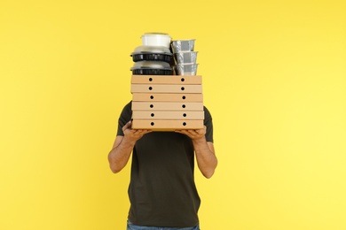 Young courier with different orders on color background. Food delivery service