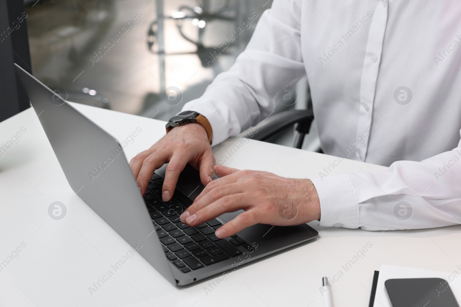 Photo of Man working on laptop at white desk in office, closeup