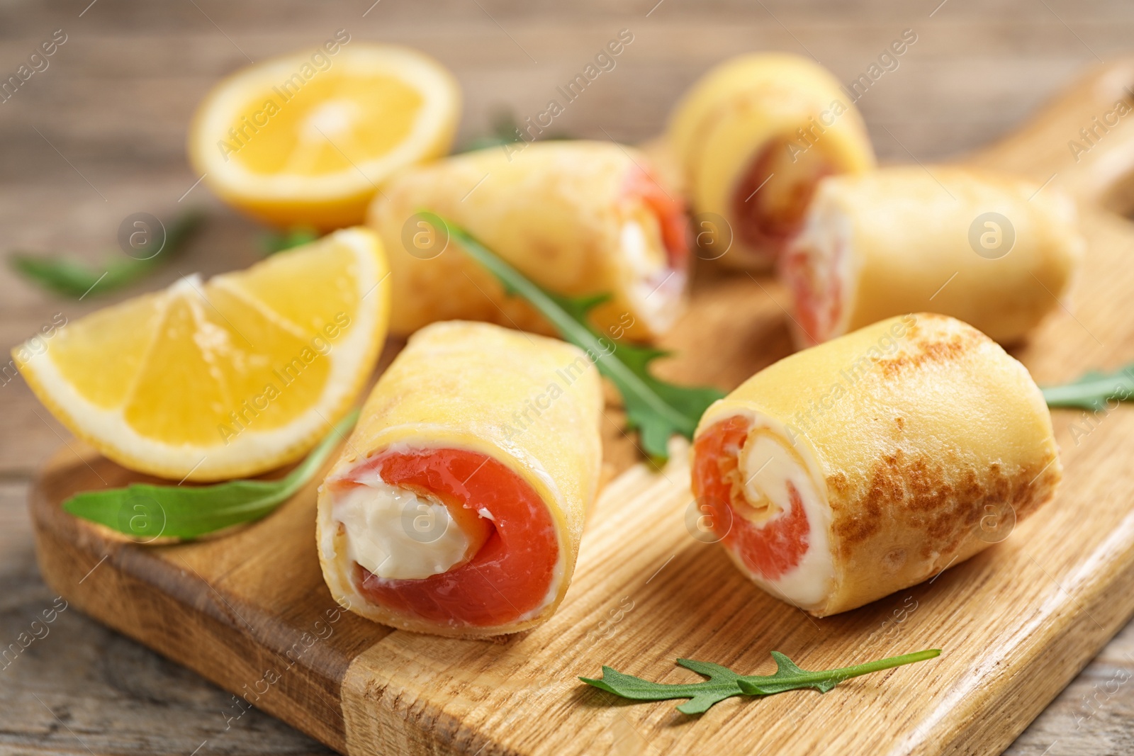 Photo of Delicious thin pancakes with salmon and cream cheese on wooden board, closeup