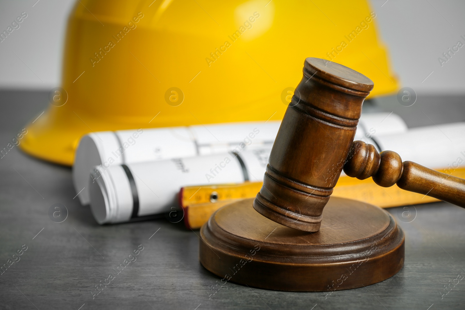 Photo of Construction and land law concepts. Judge gavel, protective helmet with drawings on grey table, closeup