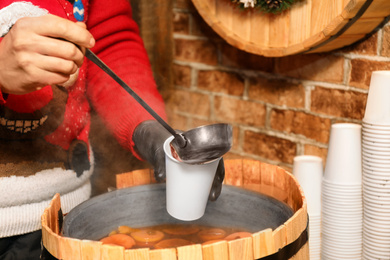 Photo of Seller pouring tasty aromatic mulled wine into cup at winter fair, closeup
