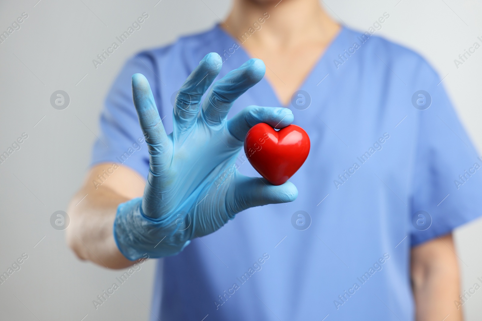 Photo of Doctor wearing light blue medical glove holding decorative heart on grey background, closeup