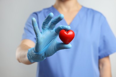 Photo of Doctor wearing light blue medical glove holding decorative heart on grey background, closeup