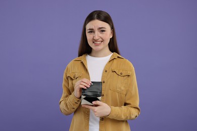 Woman showing empty wallet on purple background