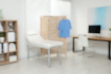 Photo of Blurred view of modern medical office with doctor's workplace and examination table in clinic