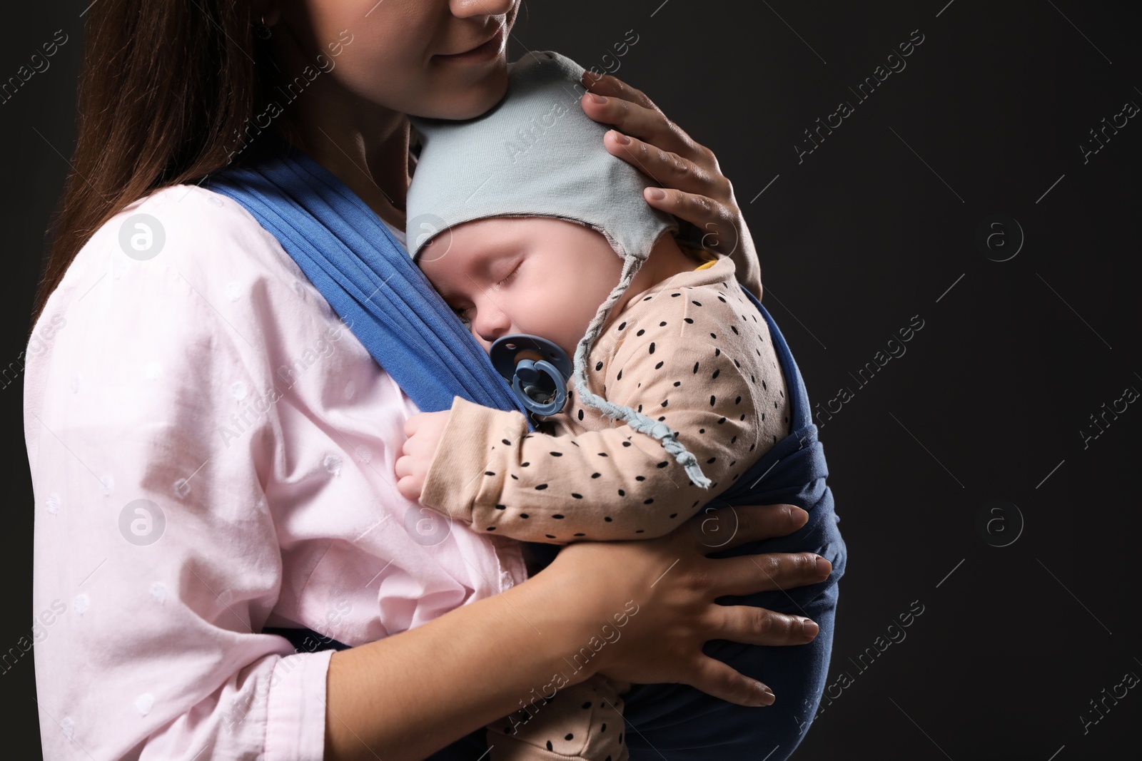 Photo of Mother holding her child in sling (baby carrier) on black background, closeup