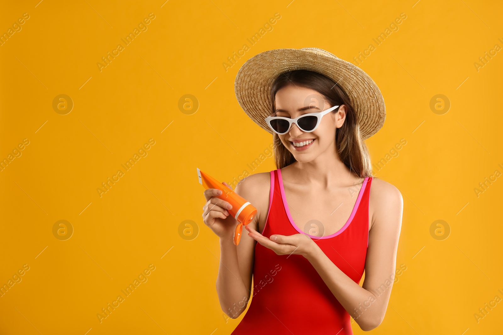 Photo of Young woman applying sun protection cream on orange background. Space for text