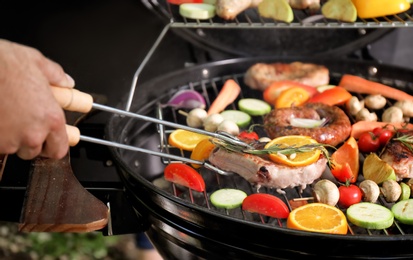 Man cooking delicious meat and vegetables on barbecue grill, closeup